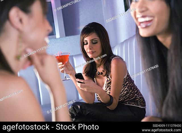 Middle Eastern woman holding cocktail and looking at cell phone