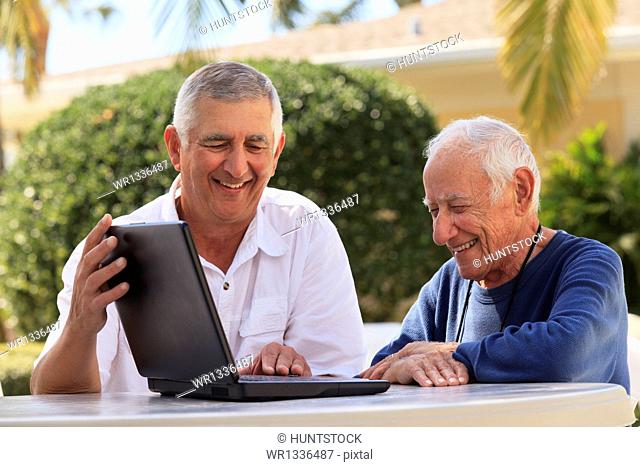 Elderly man using a laptop with his son beside him