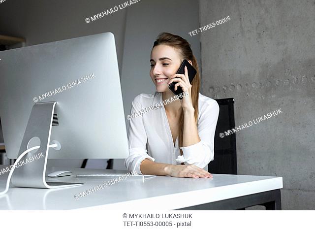 Smiling businesswoman taking phone call at desk