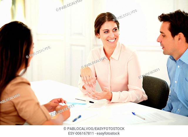 Portrait of adult professional colleagues talking and smiling while sitting on office desk