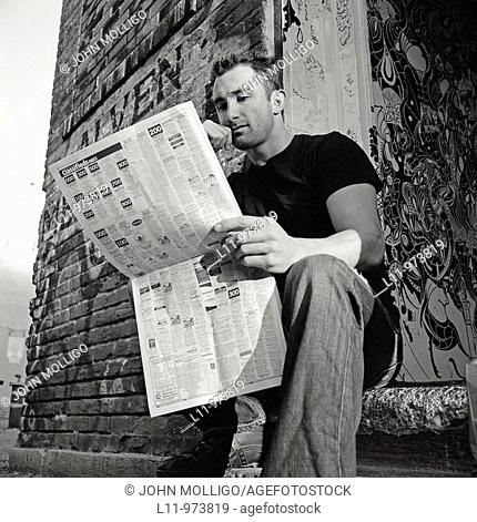 Man seated in doorway, reading a newspaper