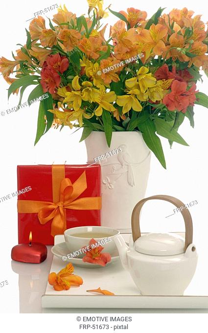 Arrangement of tea pot, a cup of tea, gift an bouquet