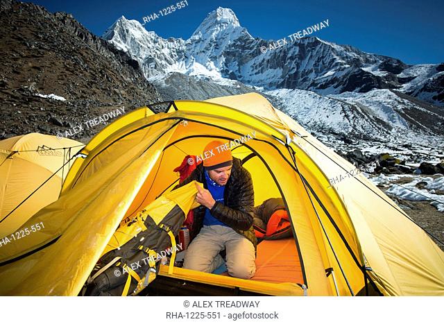 A mountaineer packs his bag in preparation to climb Ama Dablam, the 6856m peak in the distance, Khumbu Region, Himalayas, Nepal, Asia
