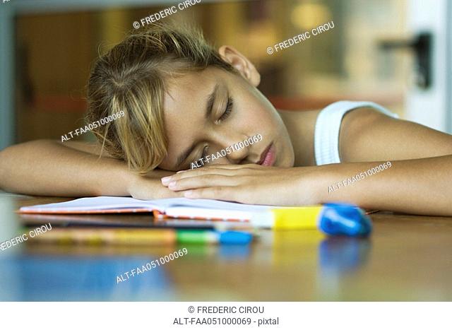 Preteen girl napping, resting head on arms laid across open book
