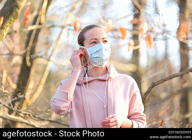 Portrait of caucasian sporty woman wearing medical protection face mask while walking in park, relaxing and listening to music