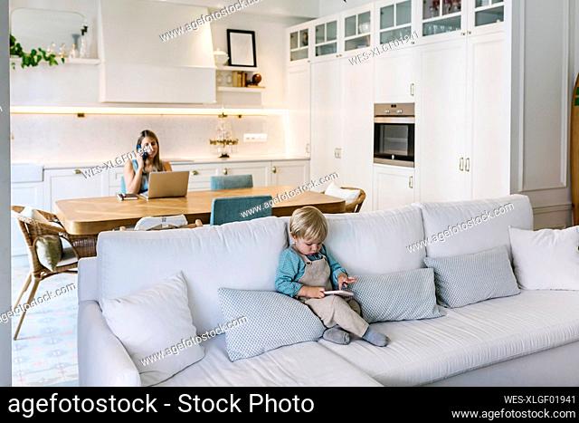 Boy using smart phone while mother working at dining table at home