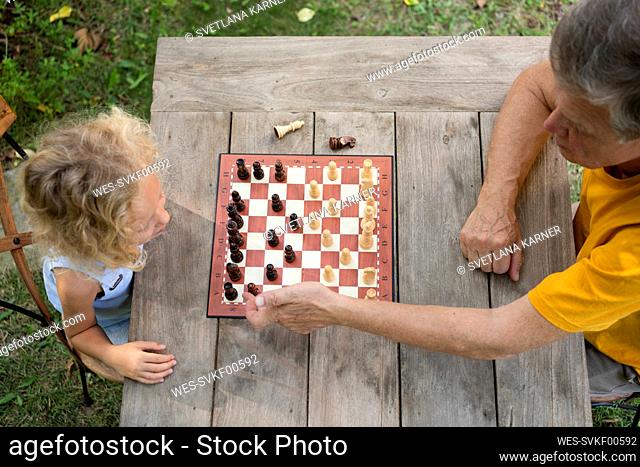 Grandfather and granddaughter playing chess on table