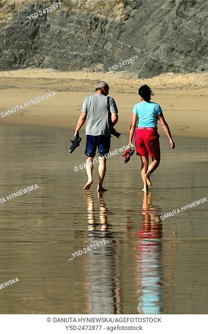 mature couple walking together on empty beach, Praia do Castelejo, Castelejo beach, near Vila Do Bispo, close to Sagres, Parque Natural do Sudoeste Alentejano e...