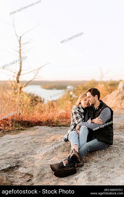 Young couple embracing on rocky surface during autumn hike