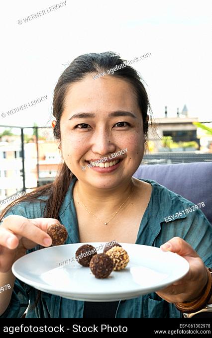 Portrait of a 32 year old Japanese woman holding a plate of round chocolates, Belgium