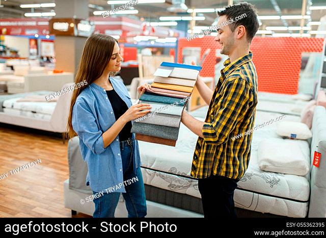 Young love couple choosing texture of mattress in furniture store showroom. Man and woman looking samples for bedroom in shop