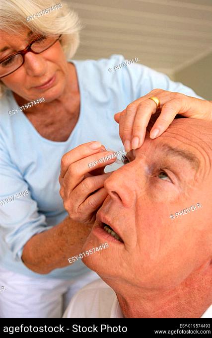 Woman applying eye drops into the eyes of elderly man