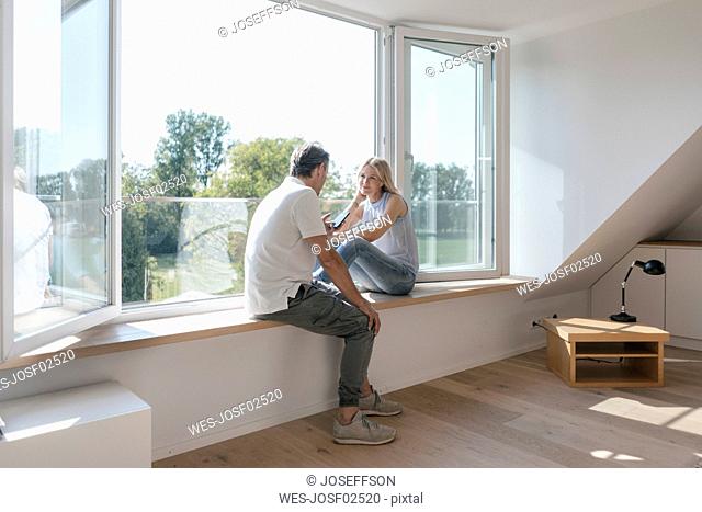 Mature couple with cell phone sitting at the window in empty room
