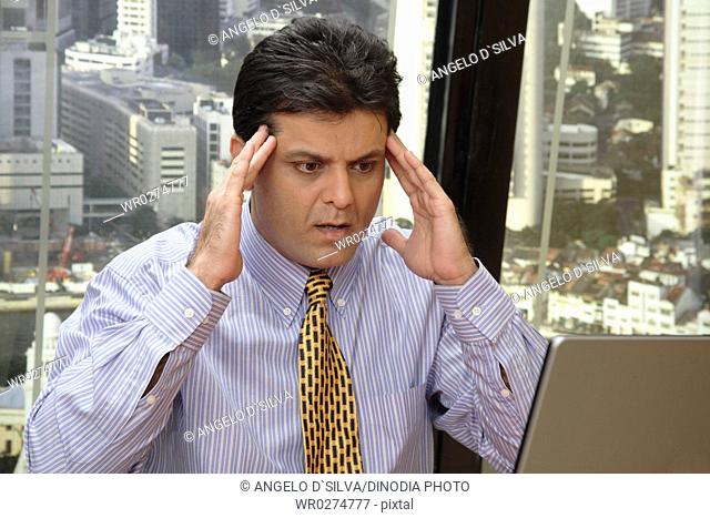 Executive looking at screen of laptop with shocked expression both hands touching forehead in office at top floors of skyscraper in modern city MR687U
