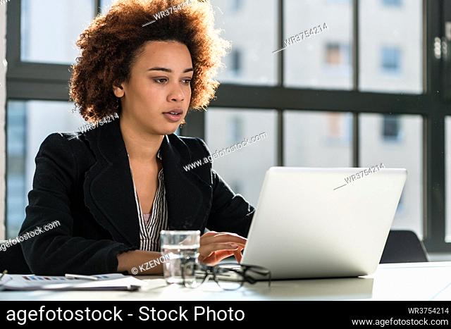 Portrait of African American woman sitting at desk while working on laptop in the office