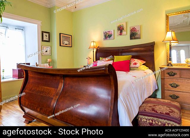 Queen size cherry wood sleigh bed and oak wood dresser in ground floor guest bedroom inside an old circa 1830 Quebecois style country home, Quebec, Canada