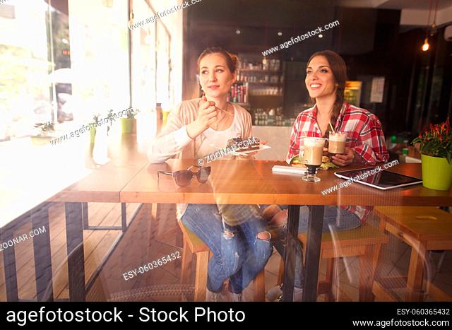 Toned picture of best friends or colleagues ladies sitting in cafe or restaurant. Women having break with sandwiches, cakes and cups of coffee