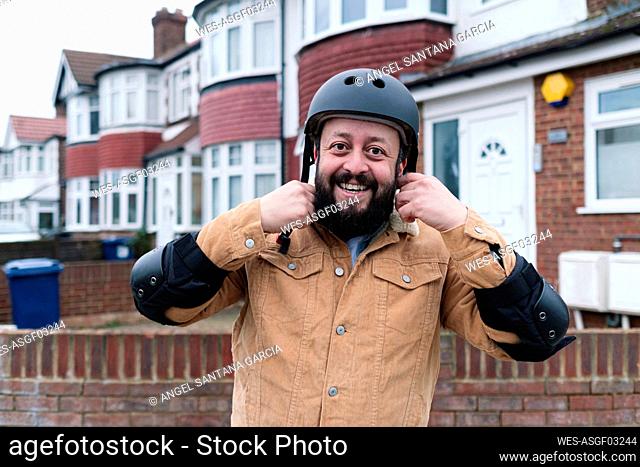Happy man adjusting helmet outside building