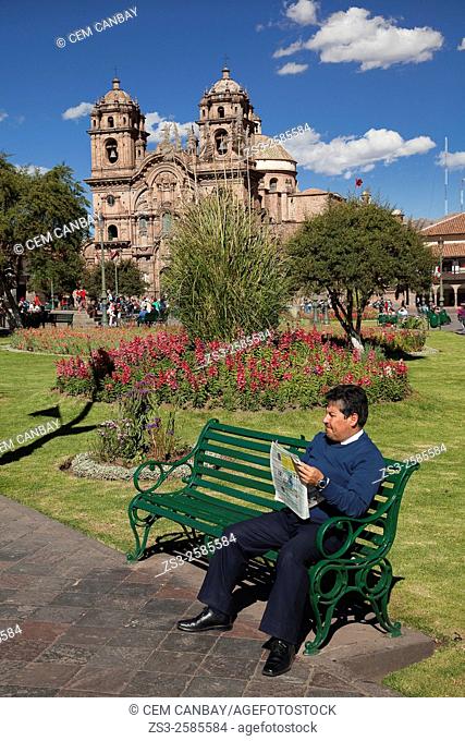 Peruvian man reading a newspaper at the park in the main square with the Cathedral at the background, Cusco, Peru, South America