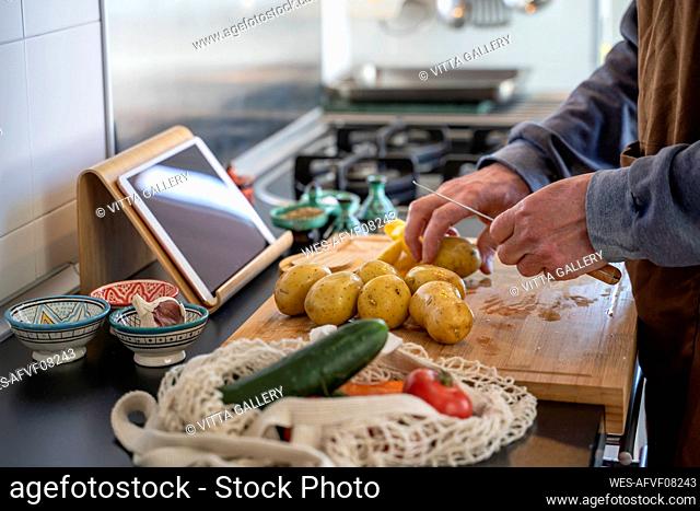 Senior man chopping potatoes on cutting board in kitchen