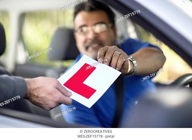 Driving instructor holding L sign in car
