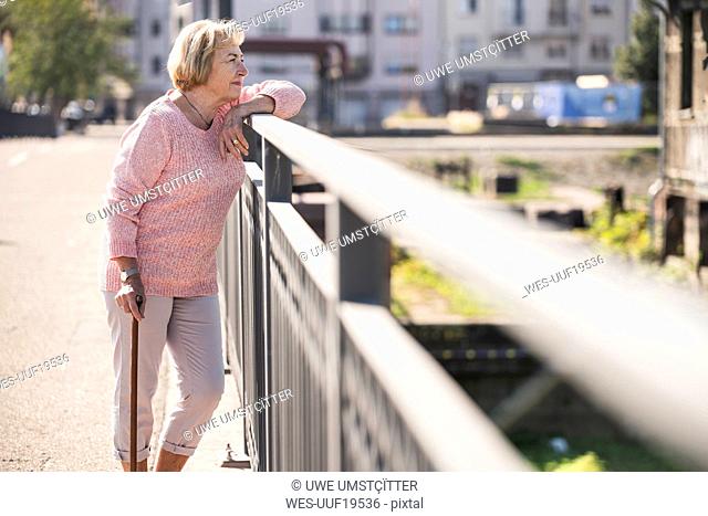 Senior woman walking on footbridge, using walking stick