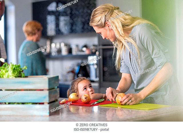 Woman preparing food in kitchen, young daughter standing at kitchen counter beside her