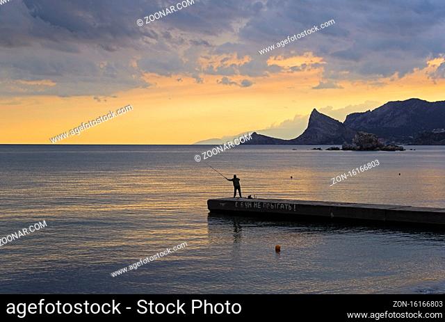 A lone fisherman on a breakwater. Evening in the Sudak bay, Crimea