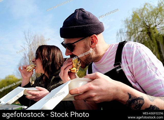 Hungry friends eating burger in park on sunny day