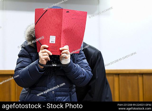 08 December 2023, Lower Saxony, Bückeburg: The defendant stands in a courtroom in Bückeburg district court before the start of the trial and holds a folder of...