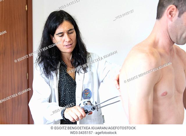 A female nutritionist measuring the body fat ratio of an athletic man by using a caliper. Plicometer