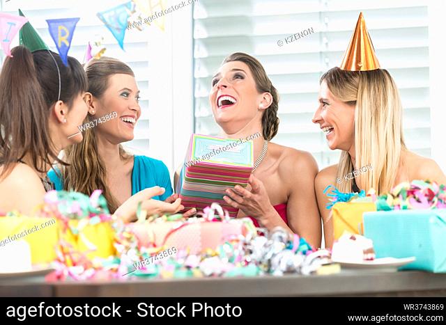 Cheerful woman holding a gift box while looking up overwhelmed by the appreciation of her best friends during a surprise birthday party at home