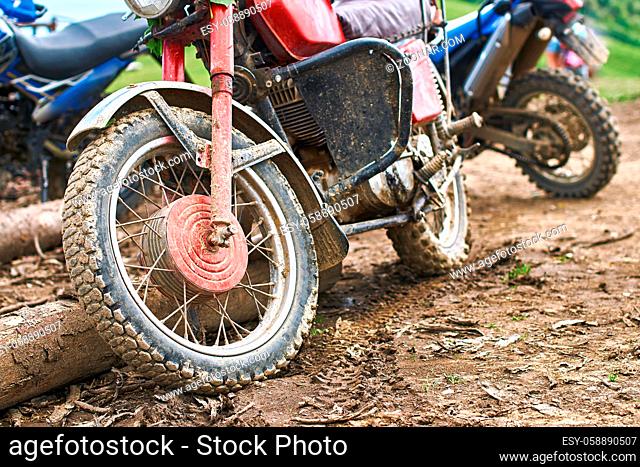 Offroad mountain motorcycles or bikes taking part in motocros competition parked on dirty terrain road with wooden logs