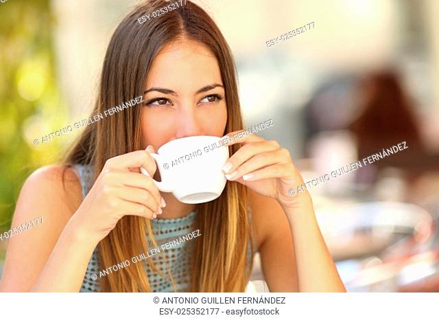 Woman drinking a coffee from a cup in a restaurant terrace while thinking and looking sideways