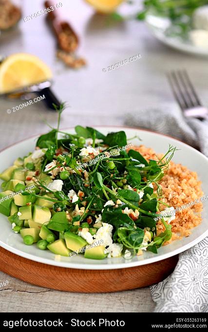 Gluten-free green vegetarian salad made of microgreen sprouts peas, avocado, quinoa, spinach, seasoned crushed almonds with slices of feta cheese