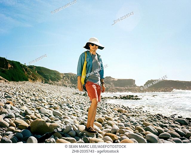 A man in summer beach wear standing on a rocky beach along the coast of Northern California's Pacific Coast Highway