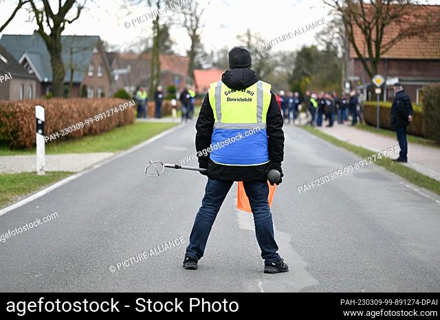 09 March 2023, Lower Saxony, Aurich: A marshal secures the road during boßeln. During traditional landscape boßeln, throwing skills can be put to the test in...