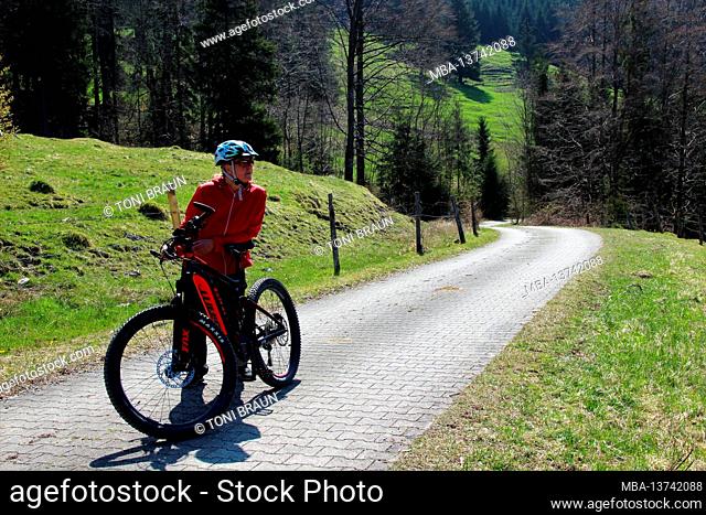 Woman on a bicycle tour with a mountain bike, ebike, e-bike Germany, Bavaria, Alpine foothills, Ohlstadt, spring, road, path, bicycle helmet, bicycle
