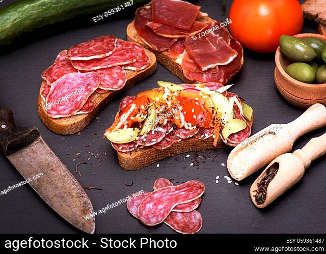 sandwiches with pieces of sausage salami and a hamon on a black background, seasoned with spices