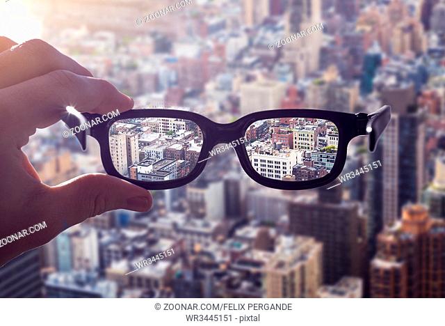 cityscape focused in glasses lenses with hand holding the eyewear between thumb and index finger