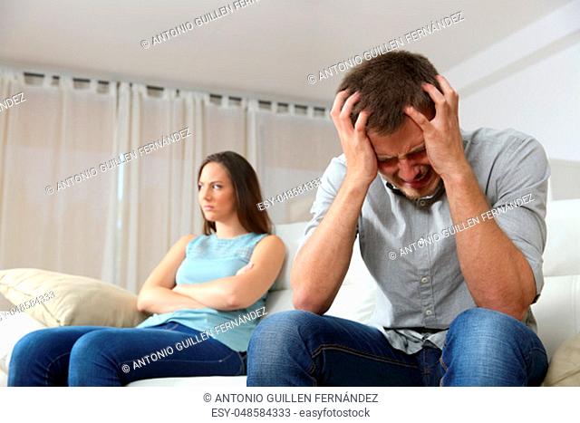 Sad man and his angry girlfriend after argument sitting on a couch at home