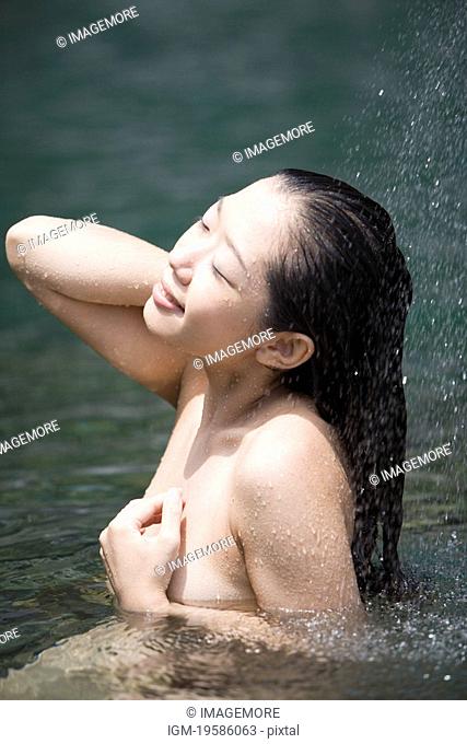 Young woman standing in water, naked, eyes closed, side view, outdoors