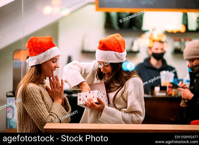 The girl gives a gift to her female friend in caffe. Portrait of happy cute young friends