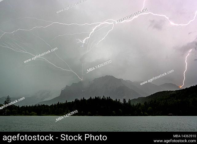 Thunderstorm lightning at the Karwendel above Mittenwald into the western Karwendelspitze. In the foreground the Lautersee and forest