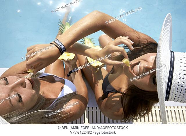 Two young women by the pool, eating pineapple. Chersonissos, Crete, Greece
