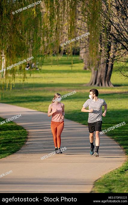 Couple wearing face masks while jogging on footpath at park
