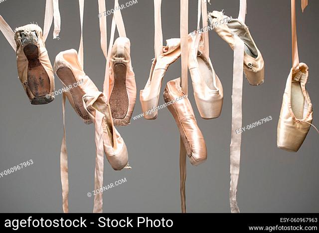 Many pairs of ballet shoes hang haphazardly on a hanger. Pointe in different condition from new to very shabby old. Horizontal