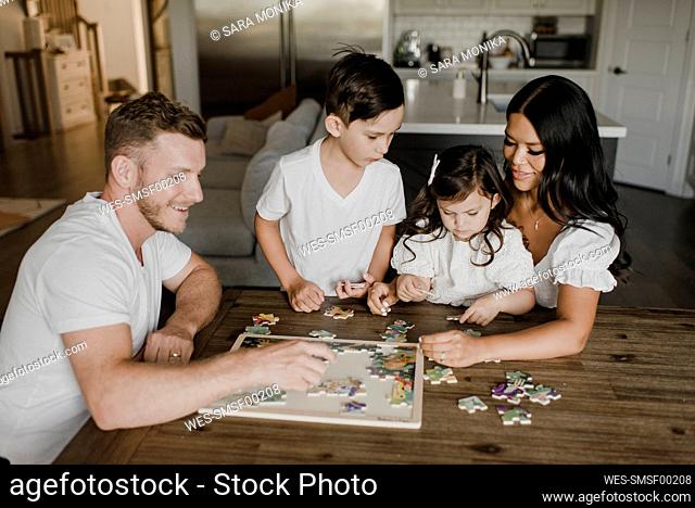 Smiling parents solving puzzle with kids over table at home