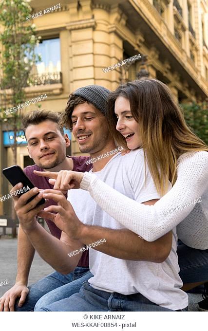 Three friends using sharing cell phone in the city