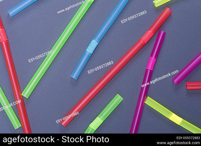 plastic multicolored straws for cocktail are scattered on a black background